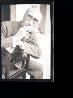 portrait photographique d'André Gide, de face, avec lunettes, cigarette à la bouche, à califourchon sur une chaise, juillet 1931