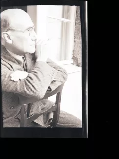 portrait photographique d'André Gide, de profil droit, avec lunettes, cigarette dans la main droite, à califourchon sur une chaise, juillet 1931