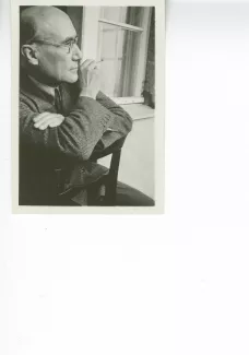 portrait photographique d'André Gide, de profil droit, avec lunettes, cigarette dans la main droite, à califourchon sur une chaise, juillet 1931
