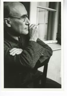 portrait photographique d'André Gide, de profil droit, avec lunettes, cigarette dans la main droite, à califourchon sur une chaise, juillet 1931