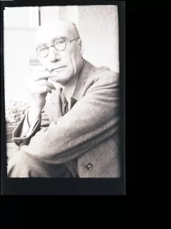 portrait photographique en buste d'André Gide, avec lunettes, regardant l'objectif, cigarette dans la main droite, le coude droit posé sur le genou, juillet 1931