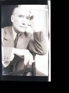 portrait photographique en buste d'André Gide, regardant l'objectif, cigarette dans la main droite, la main gauche sur le front, à califourchon sur une chaise, juillet 1931