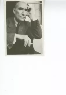 portrait photographique en buste d'André Gide, regardant l'objectif, cigarette dans la main droite, la main gauche sur le front, à califourchon sur une chaise, juillet 1931