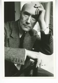 portrait photographique en buste d'André Gide, de face, regardant l'objectif, cigarette dans la main droite, la main gauche sur le front, à califourchon sur une chaise, juillet 1931