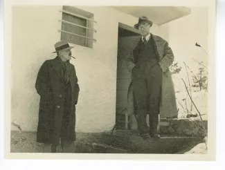 photographie d’André Gide, avec lunettes et chapeau, mains dans les poches, et Charles-Ferdinand Ramuz, devant l'entrée d'une maison, au lac de Genève, décembre 1933