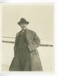 photographie d’André Gide, avec lunettes et chapeau, mains dans les poches, dans un paysage enneigé, lac de Genève, décembre 1933