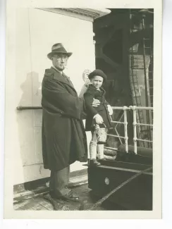 photographie d’André Gide, avec lunettes et chapeau, tenant un enfant, sur le pont d'un bateau