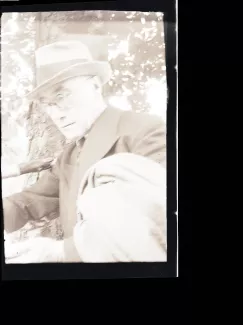 portrait photographique en buste d'André Gide, avec lunettes, chapeau et veste au bras, lisant, août 1934