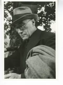 portrait photographique en buste d'André Gide, avec lunettes, chapeau et veste au bras, lisant, août 1934