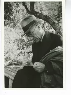 portrait photographique d'André Gide, avec lunettes, chapeau et veste au bras, lisant assis sur un banc, août 1934