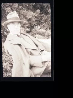 portrait photographique d'André Gide, avec lunettes et chapeau, adossé à une chaise et tourné vers l’objectif, août 1934