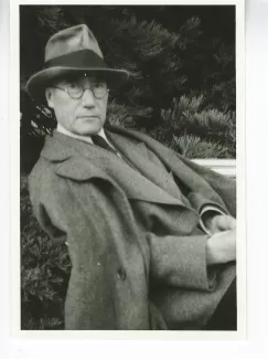 portrait photographique d'André Gide, avec lunettes et chapeau, adossé à une chaise et tourné vers l’objectif, août 1934