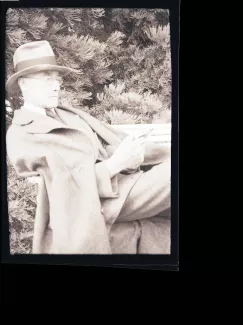 portrait photographique d'André Gide, avec lunettes et chapeau, adossé à une chaise, lisant un livre, août 1934