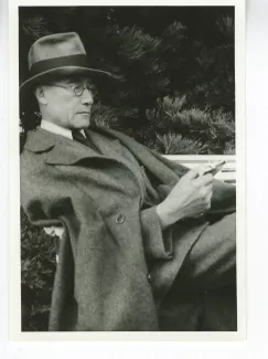 portrait photographique d'André Gide, avec lunettes et chapeau, adossé à une chaise, lisant un livre, août 1934