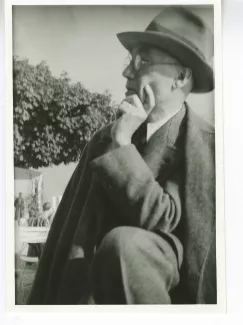 portrait photographique d'André Gide, avec lunettes et chapeau, de ¾ à gauche, la main gauche sur la joue et le coude gauche sur un genou, au bord du lac de Thoune, août 1934