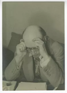 portrait photographique en buste d’André Gide, avec lunettes, assis à une table, lisant, les deux mains sur le front, au Vaneau