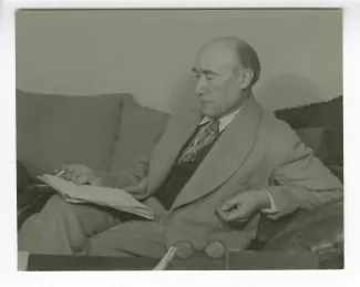 portrait photographique d’André Gide, assis sur un sofa, lisant, une cigarette dans la main droite, au Vaneau