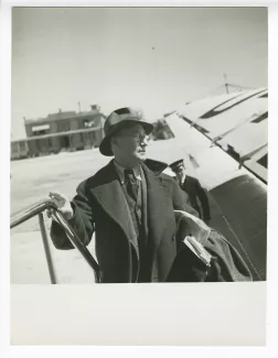 photographie d’André Gide, avec lunettes et chapeau, sur l'escalier d'embarquement d'un avion, en escale à Berlin lors du voyage Paris-Moscou, juin 1936