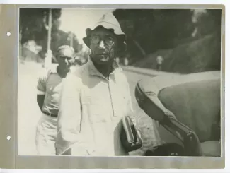 photographie d’André Gide, avec lunettes et chapeau, des livres dans la main, à côté d'une voiture, en extérieur, à Sotchi, lors du voyage en URSS, août 1936