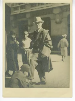 photographie en pied d’André Gide, debout, avec lunettes et chapeau, se faisant cirer les chaussures dans une rue d'Alger, 15 février 1936