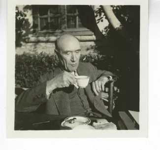 portrait photographique d’André Gide, attablé pour un petit-déjeuner en plein air, une tasse de thé à la main, octobre 1936