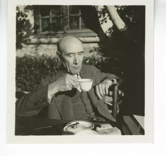 portrait photographique d’André Gide, attablé pour un petit-déjeuner en plein air, une tasse de thé à la main, octobre 1936