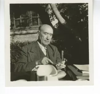 portrait photographique d’André Gide, attablé pour un petit-déjeuner en plein air, beurrant une tartine, octobre 1936