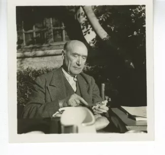 portrait photographique d’André Gide, attablé pour un petit-déjeuner en plein air, beurrant une tartine, octobre 1936