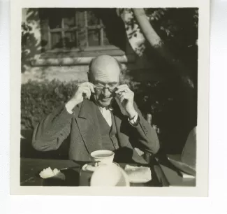 portrait photographique d’André Gide, attablé pour un petit-déjeuner en plein air, mettant ses lunettes, octobre 1936