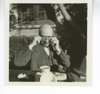 portrait photographique d’André Gide, attablé pour un petit-déjeuner en plein air, mettant ses lunettes, octobre 1936