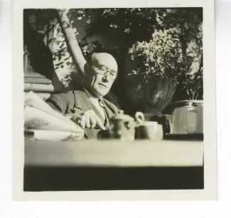 portrait photographique d’André Gide, avec lunettes, attablé pour un petit-déjeuner en plein air, le regard vers son couteau, octobre 1936