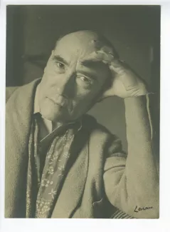 portrait photographique en buste d’André Gide, avec foulard fleuri, regardant l’objectif, la main gauche sur le front, accoudé à un sofa, au Vaneau