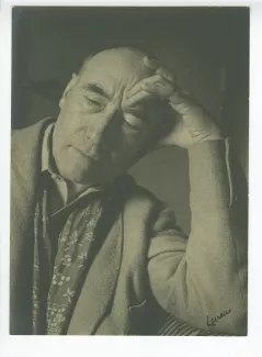 portrait photographique en buste d’André Gide, avec foulard fleuri, regardant vers le bas, la main gauche sur le front, accoudé à un sofa, au Vaneau