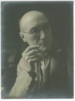 portrait photographique en buste d’André Gide, avec lunettes et foulard fleuri, de ¾ à droite, une cigarette dans la main droite, au Vaneau