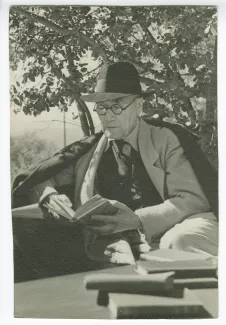 portrait photographique d’André Gide, avec lunettes et chapeau, lisant sur une terrasse chez Marie de Saint-Exupéry, été 1941