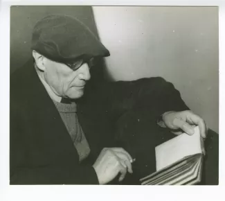 portrait photographique en buste d’André Gide, avec lunettes et béret, de profil, lisant et fumant, mars 1944
