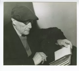 portrait photographique en buste d’André Gide, avec lunettes et béret, de profil, lisant et fumant, mars 1944