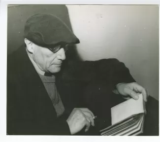 portrait photographique en buste d’André Gide, avec lunettes et béret, de profil, lisant et fumant, mars 1944