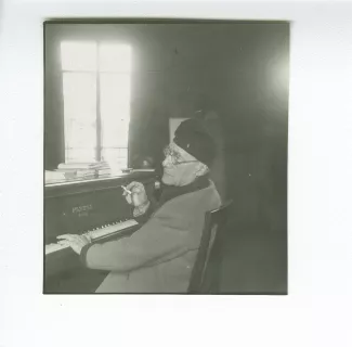 portrait photographique d’André Gide, avec lunettes et bonnet, de dos, au piano, fumant, au Vaneau