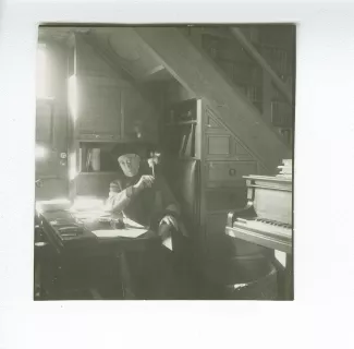 portrait photographique d’André Gide, avec lunettes et bonnet, assis à son bureau, regardant ses papiers tout en fumant, au Vaneau