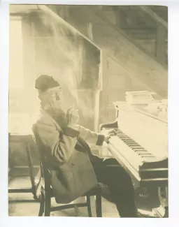 portrait photographique d’André Gide, avec lunettes et bonnet, assis à son piano, fumant, au Vaneau
