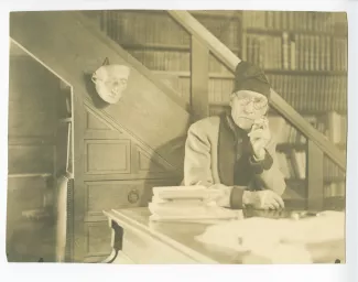 portrait photographique d’André Gide, avec lunettes et bonnet, accoudé à son piano, de face, fumant, au Vaneau