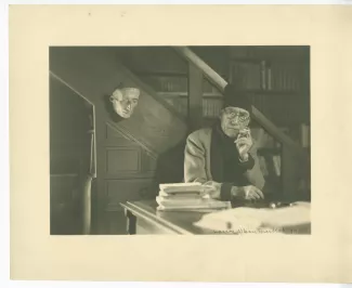 portrait photographique d’André Gide, avec lunettes et bonnet, accoudé à son piano, de face, fumant, au Vaneau