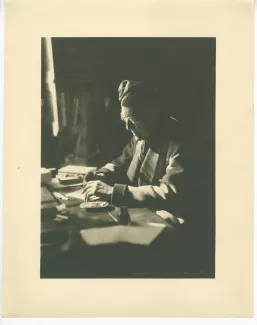 portrait photographique d’André Gide, avec lunettes et bonnet, assis à son bureau, écrivant et fumant, au Vaneau