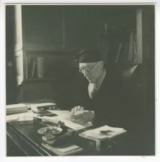 portrait photographique d’André Gide, avec lunettes et bonnet, assis à son bureau, lisant, au Vaneau