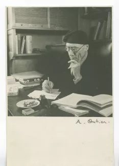 portrait photographique d’André Gide, avec lunettes et bonnet, assis à son bureau, écrivant, la main sur la joue, au Vaneau