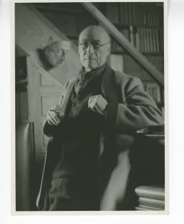 portrait photographique d’André Gide, avec lunettes, debout, de face, accoudé à son piano, au Vaneau