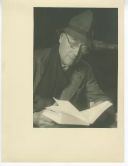 portrait photographique en buste d’André Gide, avec lunettes et chapeau, lisant un livre