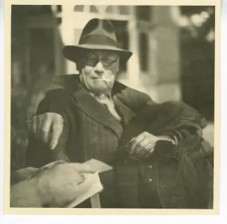 photographie d’André Gide, avec lunettes et chapeau, montrant quelque chose à son voisin sur une page volante de livre, en extérieur, château de Bussigny, août 1946