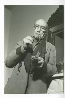 portrait photographique d’André Gide, avec lunettes, près d'un miroir, s'allumant une cigarette, cravate dénouée, chez Richard Heyd, hiver 1947